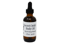 photo of secret order body oil packaged in 2 oz glass dropper bottle with white label that reads Secret Order Body Oil. Fig & Deep Woods.