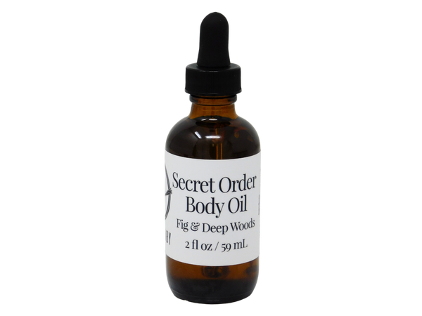 photo of secret order body oil packaged in 2 oz glass dropper bottle with white label that reads Secret Order Body Oil. Fig & Deep Woods.