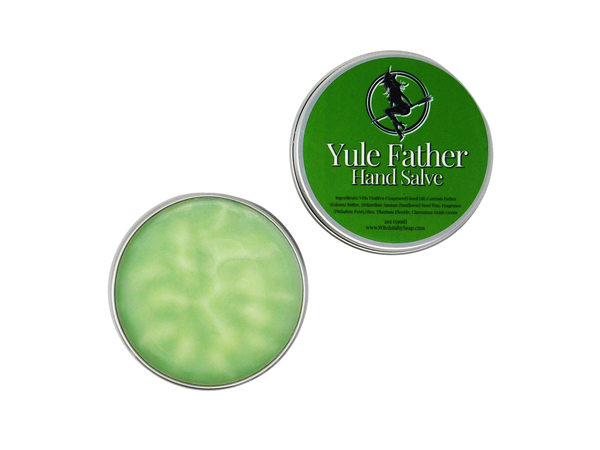 Yule Father Hand Salve pictures on white background with lid off and displayed beside it. Moisturizing holiday evergreen colored salve is packaged in a tin container. Green label on lid reads Yule Father hand Salve with ingredients.